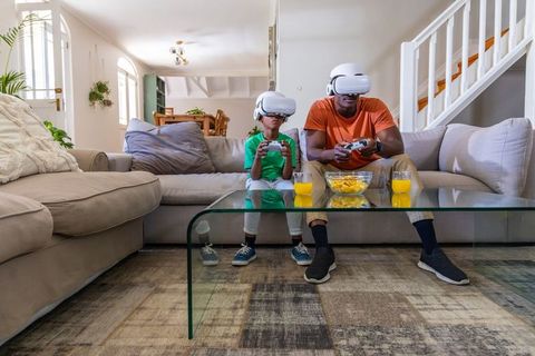 Black dad and son in VR headsets gaming together on living room couch