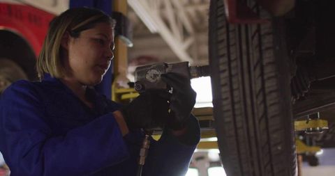 Mechanic Tightening Lug Nuts with Impact Wrench Under Lifted Car in Garage