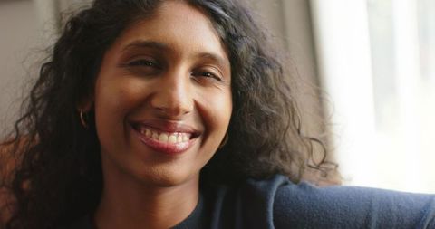 Smiling woman leaning on sofa in natural light, closeup with curly hair and gold hoops