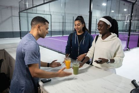 Ordering smoothies at sports club counter, friends collecting healthy drinks after match
