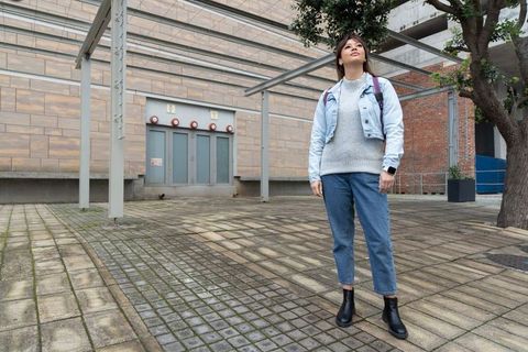 Asian woman standing in urban plaza looking up and checking smartwatch with purple backpack