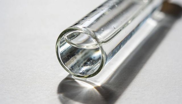 Clear glass tube macro with caustic light reflections and specular highlights on white surface