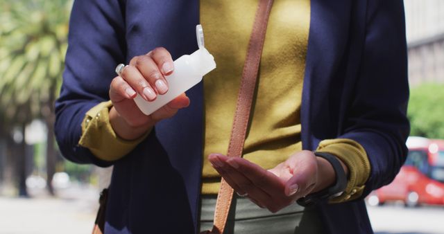 Person applying hand sanitizer outdoors in sunny weather, ensuring hygiene and cleanliness. Can be used for health and safety campaigns, personal care product promotions, or illustrating preventive measures against germs.