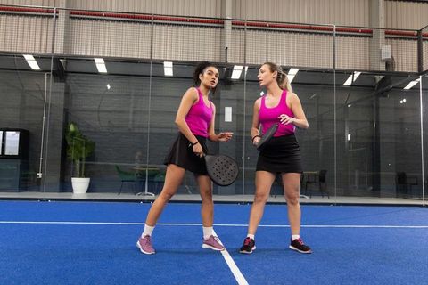 Female padel doubles playing on blue indoor court wearing magenta tops and black skorts