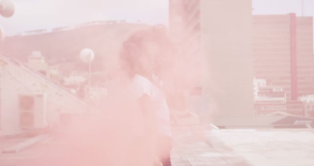 A young biracial woman stands enveloped in a hazy pink mist, with copy space. Captured outdoors, the image evokes a dreamy, ethereal atmosphere.