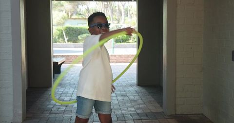African american boy spinning neon hula hoop in brick courtyard corridor wearing sunglasses