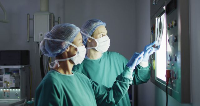 Two surgeons in an operating room are using advanced surgical equipment. Both are wearing surgical masks and sterile gowns. This image can be used for health care advertisements, medical articles, educational materials on surgery, or illustrating the use of technology in modern healthcare settings.