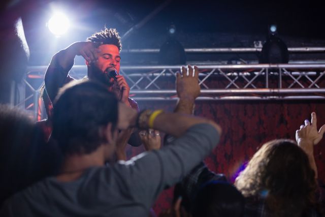 This image captures a dynamic moment of a singer performing at a nightclub. The vibrant scene features the artist passionately singing into the microphone while engaging with an enthusiastic audience. Ideal for use in promotions for live music events, nightlife advertisements, concert announcements, and entertainment-related content.