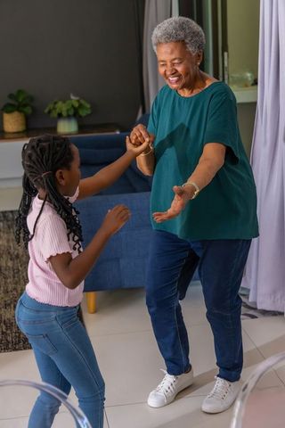 African american grandmother dancing with granddaughter in living room sharing joyful bond