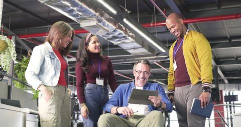 Multiracial team collaborating with wheelchair user reviewing tablet in modern open office