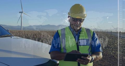 Wind farm technician monitoring turbine performance on tablet near service vehicle desert