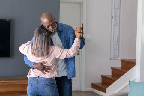 Mature diverse couple slow dancing and embracing in cozy modern living room