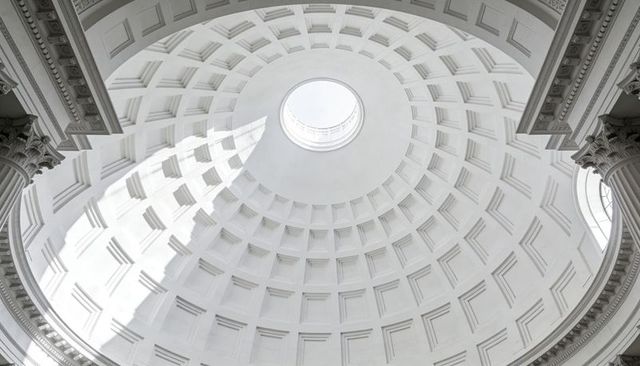 Sunlit neoclassical coffered dome with oculus and fluted columns in symmetrical rotunda
