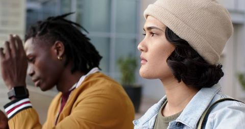 Young woman gazing thoughtfully on urban campus bench wearing beanie and denim jacket