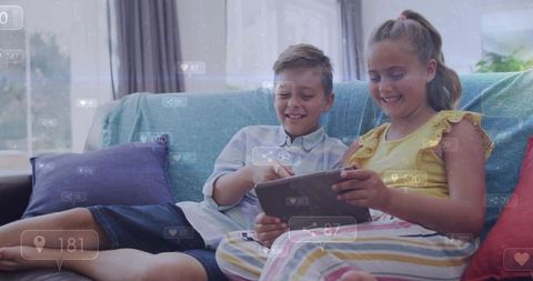 Brother and sister sharing tablet on sofa playing app and laughing together at home
