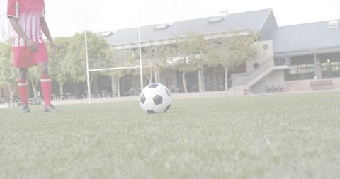 Resting soccer ball on school turf with player in red-and-white kit near goalposts