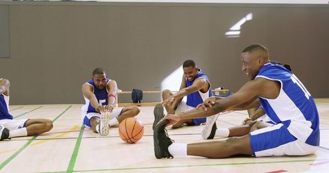 Black basketball team warming up with stretches on indoor court before practice