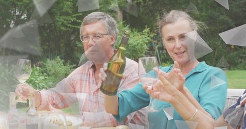Mature couple toasting with white wine on garden patio during relaxed outdoor dinner party
