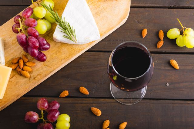 High angle view of cheese with grapes and red wine on wooden table. Ideal for use in food and drink blogs, gourmet recipe websites, restaurant menus, and culinary magazines. Perfect for illustrating articles about wine and cheese pairings, rustic dining, and elegant appetizers.