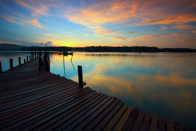 Sunset over a calm lake with vibrant colors reflected in water, featuring a wooden dock extending into the lake. Ideal for backgrounds, travel blogs, inspirational posters, or relaxation-themed projects.