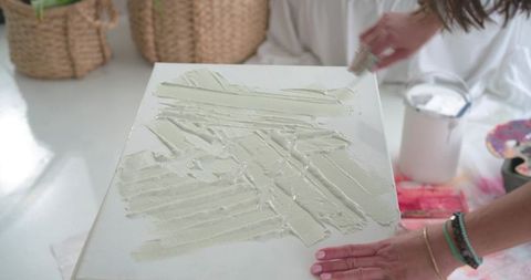 Artist spreading texture paste on canvas with palette knife in bright studio