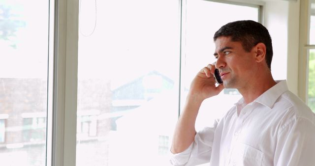 Businessman Talking on Phone by Window in Office - Download Free Stock Images Pikwizard.com