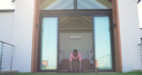 African-american woman working out at home doorway with dumbbells and laptop