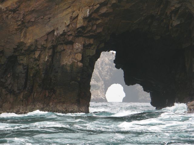 Depicts weathered sea arch with turbulent ocean waters, showing coastal rock formation. Ideal for geology studies, nature tourism ads, and coastal erosion visuals.