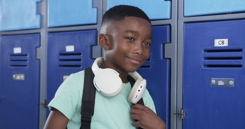 Confident african american student wearing headphones with backpack at blue school lockers