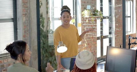 Woman presenting code on glass board in modern coworking office during team brainstorming
