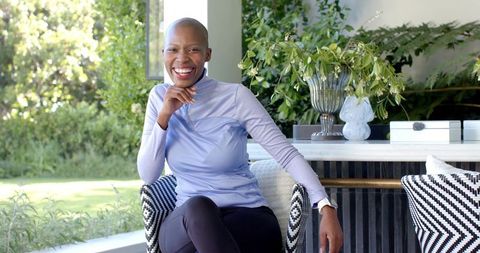 Confident bald african woman smiling on sunlit patio wearing lavender top and smartwatch