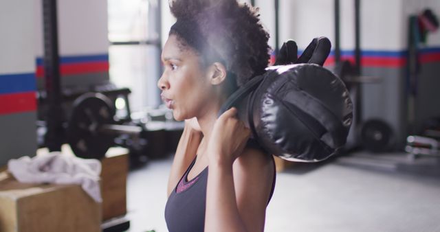 Image of determined african american woman doing squats holding sandbag weight at a gym. Exercise, fitness and healthy lifestyle.