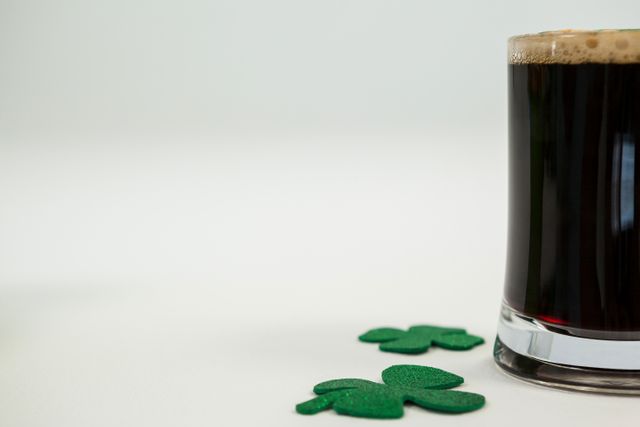 This image features a mug of black beer with foam on top, accompanied by green shamrock decorations on a white background. Ideal for use in St. Patrick's Day promotions, Irish-themed events, pub advertisements, holiday greeting cards, and festive social media posts.