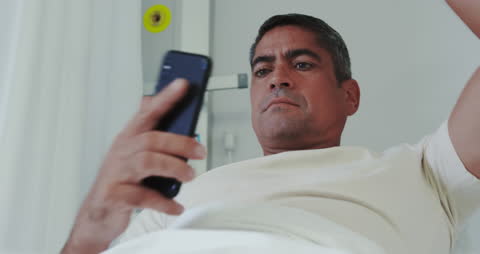 Man Relaxing in Hospital Bed Using Smartphone
