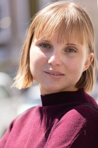 Young woman smiling and posing in urban close-up wearing burgundy sweater and nose hoop