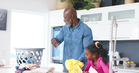 African american father teaching daughter folding laundry together in bright kitchen