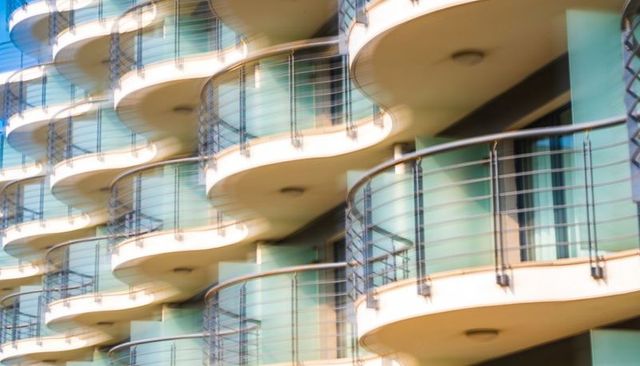 Rhythmic curved balconies stacking on midrise facade with glass doors and metal railings