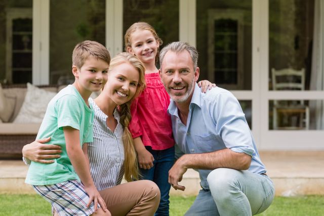 Family of four posing together in garden, smiling and showing affection. Ideal for use in family-oriented advertisements, lifestyle blogs, and promotional materials for family services or products.