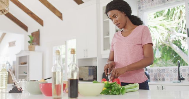 Woman cutting fresh vegetables on a kitchen counter in a well-lit modern kitchen setting. Ideal for use in blogs or websites focused on healthy eating, cooking tutorials, recipes, home lifestyles, or product advertisements related to kitchenware and home appliances.