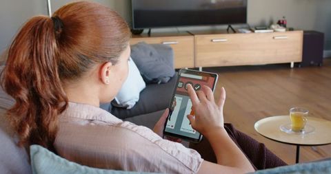 Young woman using tablet on sofa at home relaxing with tea in modern living room