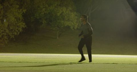 African american man practicing ball tosses on floodlit field at night building teamwork