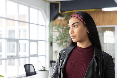Young professional woman standing by sunlit grid windows in modern coworking space
