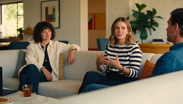 Three friends talking on sofa in modern living room, woman in stripes gesturing