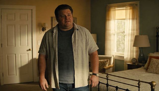 Middle-aged man standing in cozy sunlit bedroom near metal bed frame