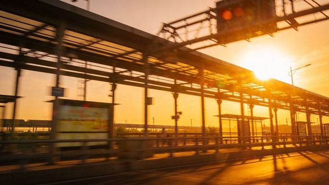 Golden-hour urban transit platform casting lens flare and silhouetting steel canopy