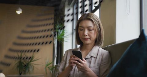 Asian Businesswoman Engaged with Smartphone in Modern Office Lounge