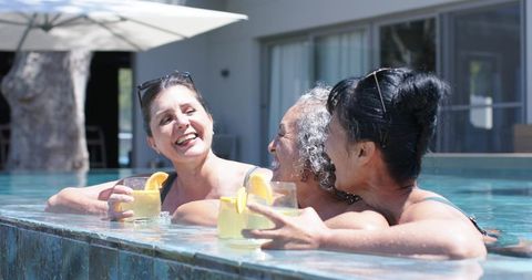 Three women relaxing in pool enjoying citrus cocktails and sunny resort friendship