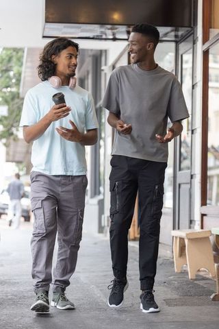 Multicultural men walking and chatting on urban sidewalk holding coffee and headphones