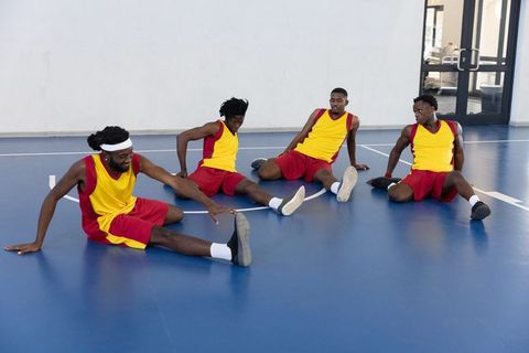 Basketball Teammates Stretching on Indoor Court Before Game