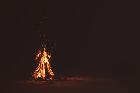 Solitary bonfire burning on sandy beach at night with glowing embers and sparks